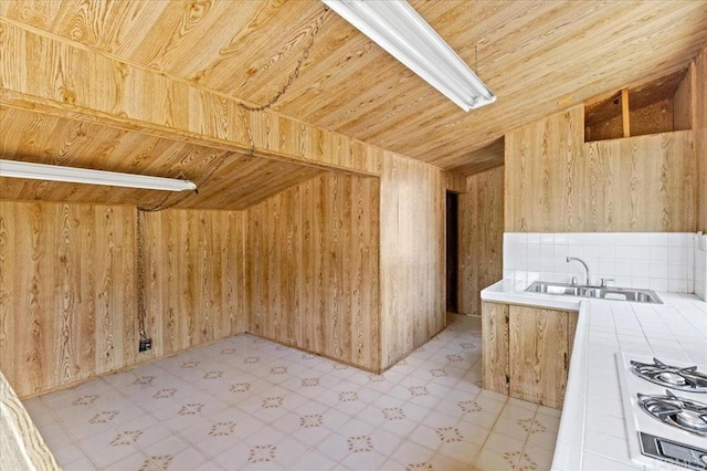 interior space with tile countertops, white gas stovetop, wood ceiling, a sink, and wooden walls