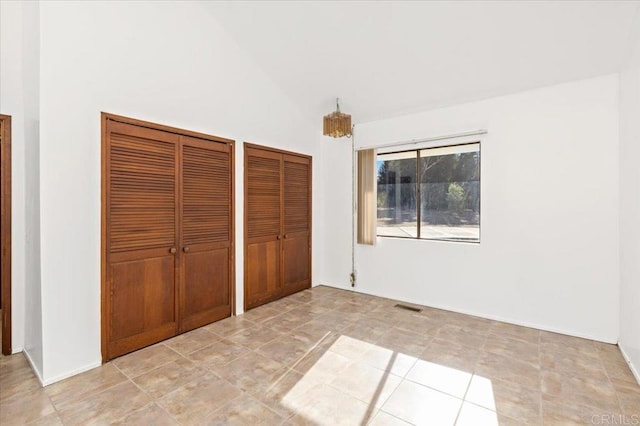 unfurnished bedroom featuring baseboards, visible vents, vaulted ceiling, and two closets