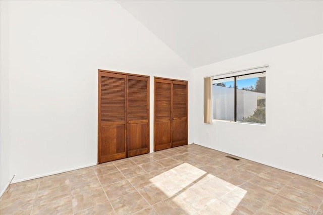 unfurnished bedroom featuring multiple closets, visible vents, and high vaulted ceiling