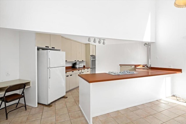 kitchen featuring light tile patterned floors, dark countertops, cream cabinets, white appliances, and a peninsula