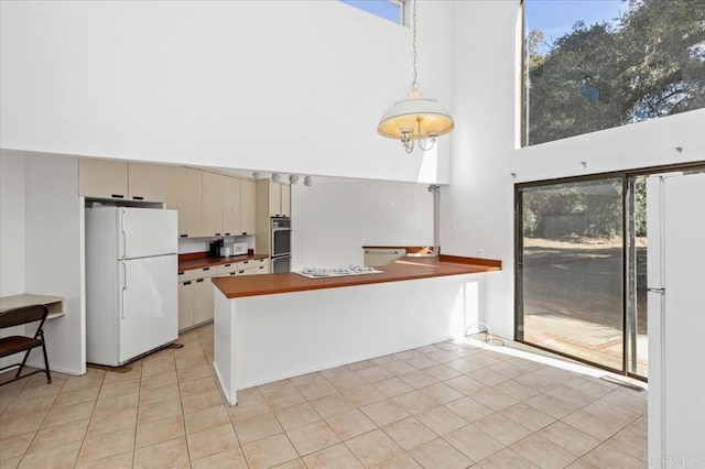 kitchen with a peninsula, white appliances, a high ceiling, and light tile patterned floors