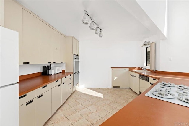 kitchen with cream cabinets, light tile patterned flooring, a sink, track lighting, and white appliances