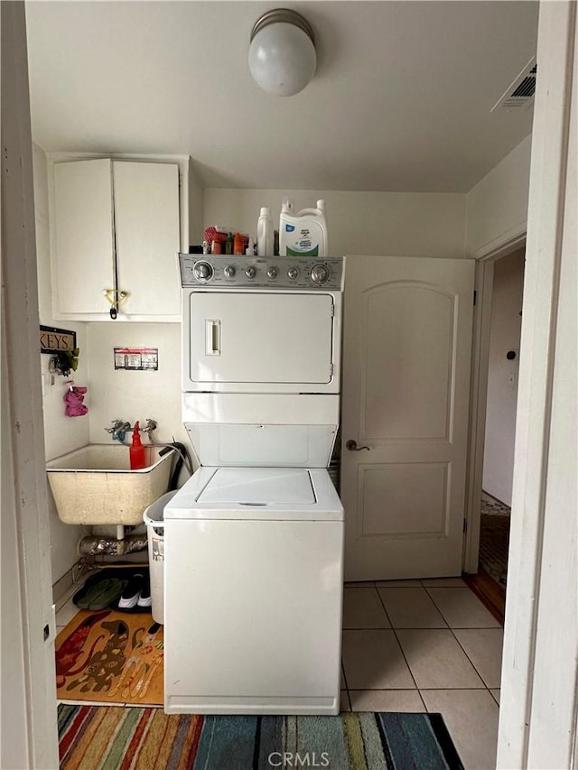 laundry room featuring cabinets, light tile patterned floors, stacked washer / dryer, and sink