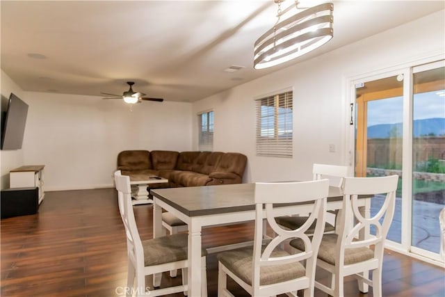 dining area featuring dark wood-type flooring, ceiling fan with notable chandelier, and a mountain view