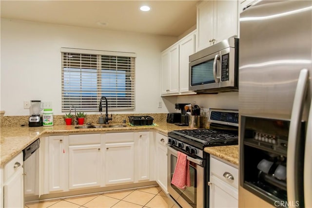 kitchen with sink, light tile patterned floors, appliances with stainless steel finishes, white cabinets, and light stone counters