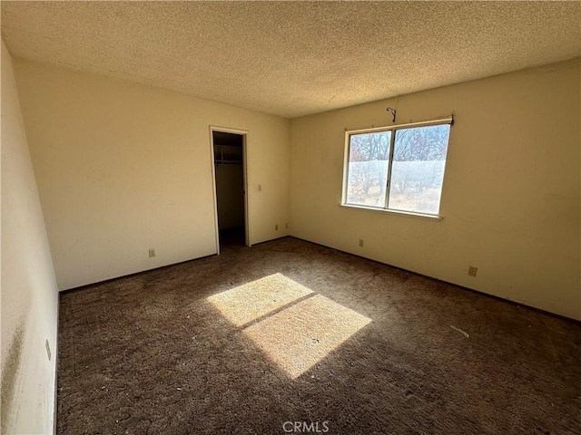 unfurnished bedroom with a spacious closet, a closet, dark carpet, and a textured ceiling