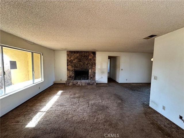 unfurnished living room featuring a stone fireplace, a textured ceiling, and dark colored carpet