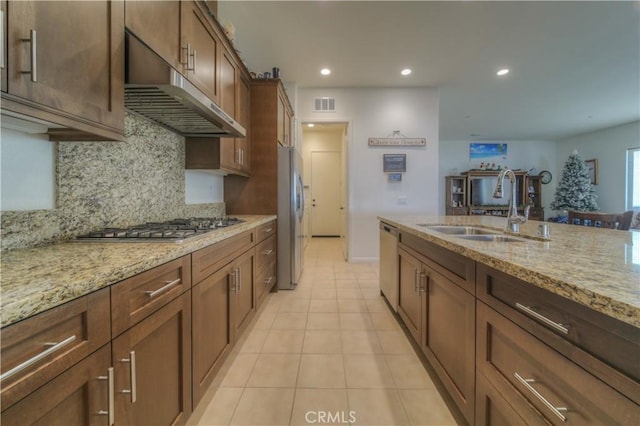 kitchen with appliances with stainless steel finishes, light stone countertops, light tile patterned flooring, backsplash, and sink