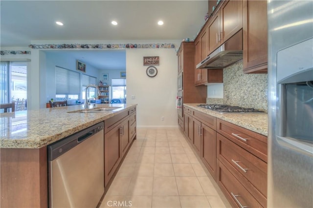 kitchen featuring sink, a center island with sink, stainless steel appliances, and light stone counters