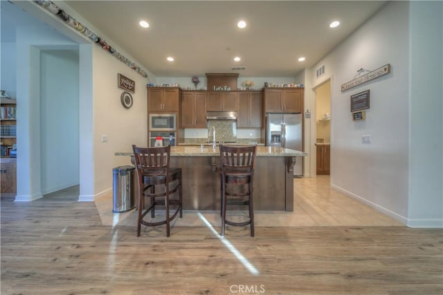 kitchen featuring a center island with sink, sink, light stone counters, stainless steel appliances, and a breakfast bar area