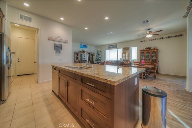 kitchen featuring an island with sink, light stone countertops, sink, ceiling fan, and appliances with stainless steel finishes