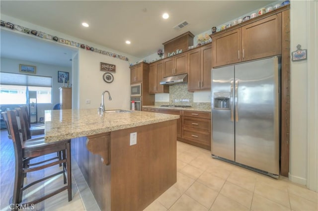 kitchen with a kitchen bar, sink, backsplash, stainless steel appliances, and an island with sink