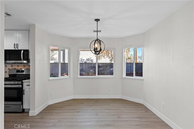 unfurnished dining area featuring an inviting chandelier, a wealth of natural light, and light hardwood / wood-style flooring