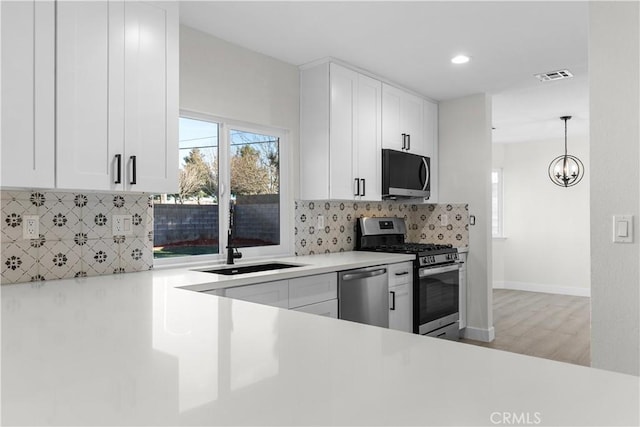 kitchen featuring appliances with stainless steel finishes, tasteful backsplash, hanging light fixtures, a chandelier, and white cabinets