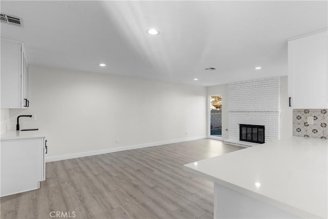 unfurnished living room featuring a fireplace, light hardwood / wood-style flooring, and sink