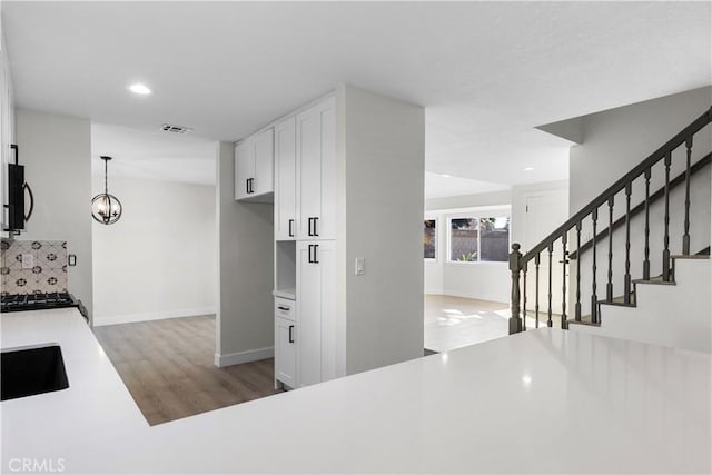 kitchen featuring decorative backsplash, sink, white cabinetry, light hardwood / wood-style flooring, and hanging light fixtures