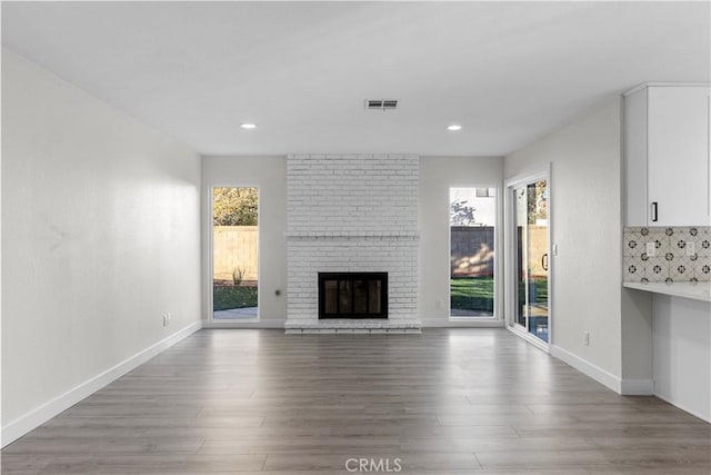 unfurnished living room featuring a brick fireplace, a healthy amount of sunlight, and hardwood / wood-style floors