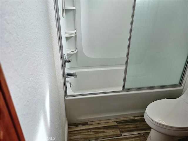 bathroom with hardwood / wood-style flooring, toilet, and shower / bath combination with glass door