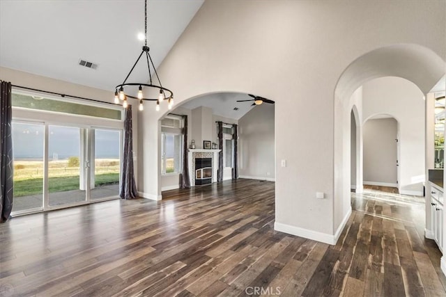 unfurnished living room with high vaulted ceiling, dark wood-type flooring, and ceiling fan with notable chandelier