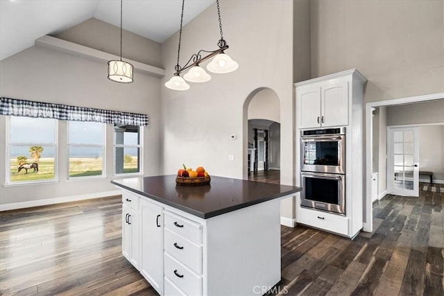 kitchen featuring a high ceiling, stainless steel double oven, a center island, decorative light fixtures, and white cabinetry