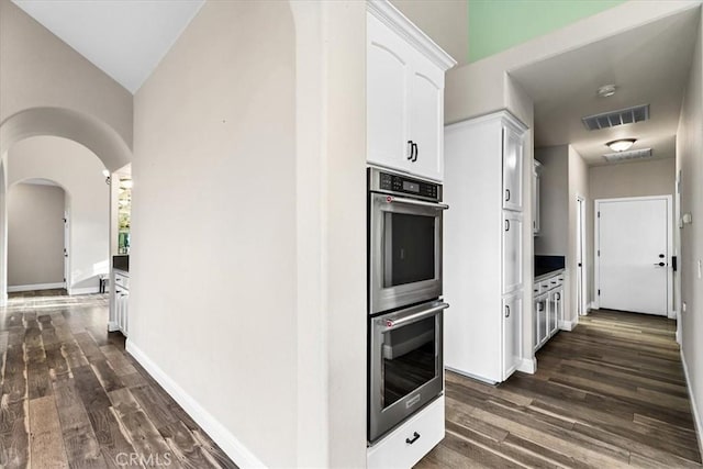 kitchen featuring stainless steel double oven, white cabinets, dark hardwood / wood-style floors, and lofted ceiling