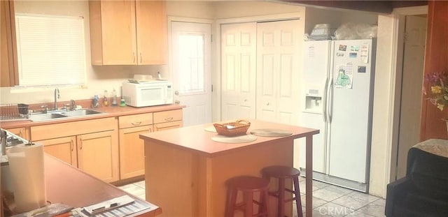 kitchen with white appliances, a kitchen island, light brown cabinets, sink, and light tile patterned flooring