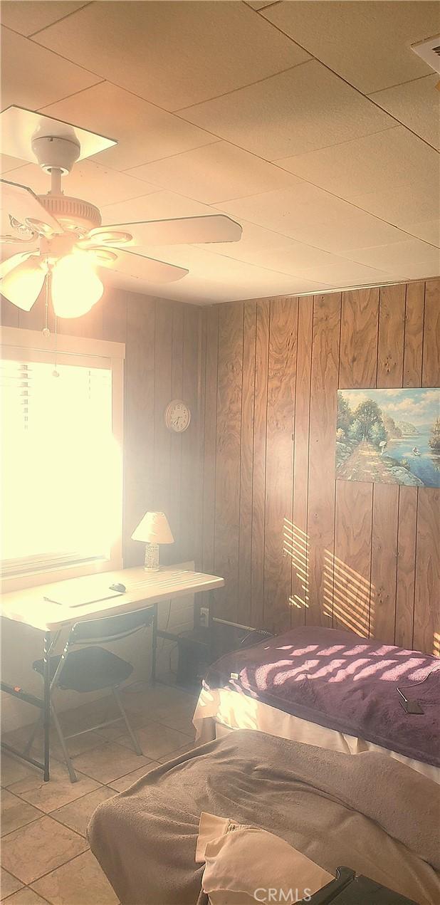 interior space featuring ceiling fan, tile patterned flooring, and wooden walls