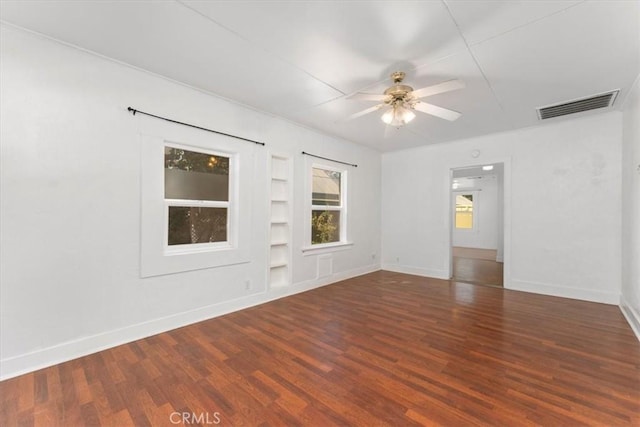 spare room featuring ceiling fan, built in shelves, and dark wood-type flooring