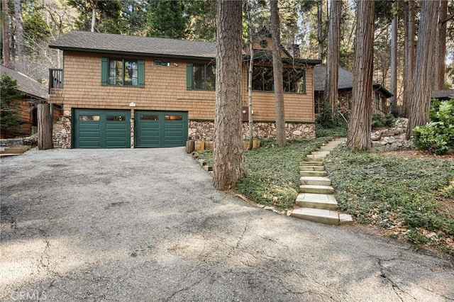 view of front of home featuring a garage, driveway, a shingled roof, and stone siding