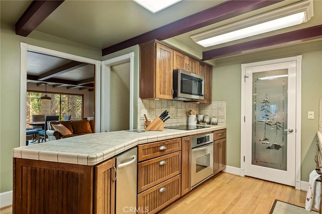 kitchen with appliances with stainless steel finishes, decorative backsplash, tile counters, light hardwood / wood-style flooring, and beamed ceiling