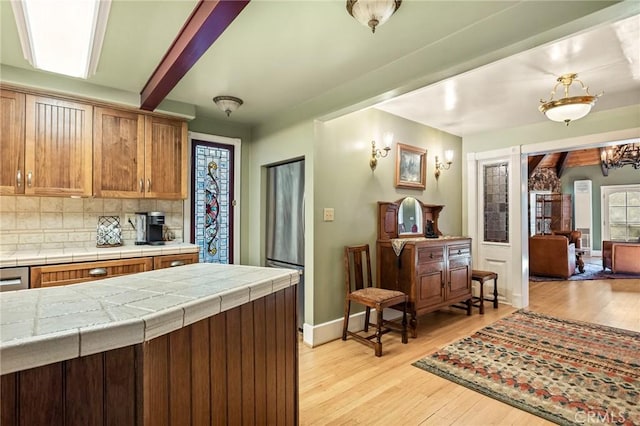 kitchen with backsplash, beamed ceiling, light wood-type flooring, tile counters, and a chandelier