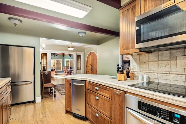 kitchen featuring appliances with stainless steel finishes, light hardwood / wood-style flooring, tile countertops, and tasteful backsplash