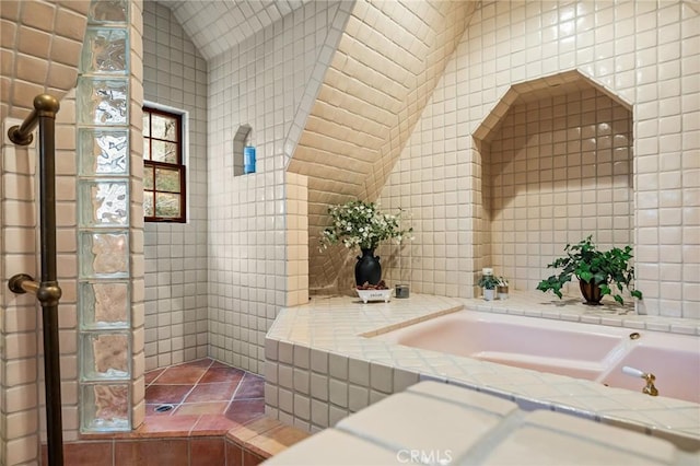 bathroom with vaulted ceiling, tile walls, and a tub to relax in