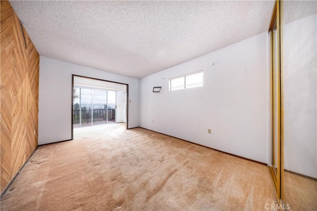 empty room with a textured ceiling, light carpet, and wooden walls