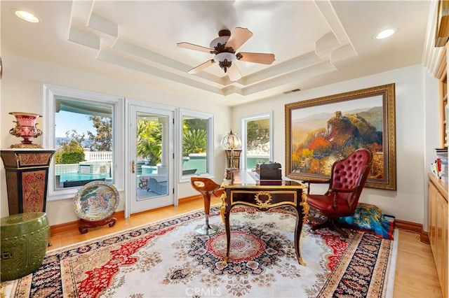 home office with light hardwood / wood-style flooring, ceiling fan, and a raised ceiling