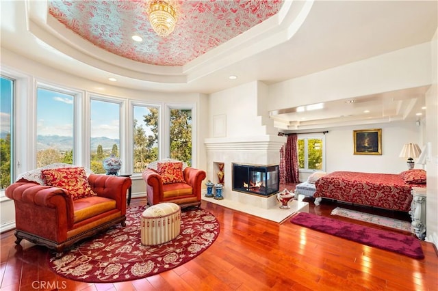 bedroom featuring a multi sided fireplace, hardwood / wood-style flooring, and a raised ceiling