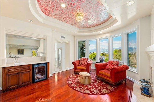 sitting room with wet bar, a wealth of natural light, beverage cooler, and a raised ceiling