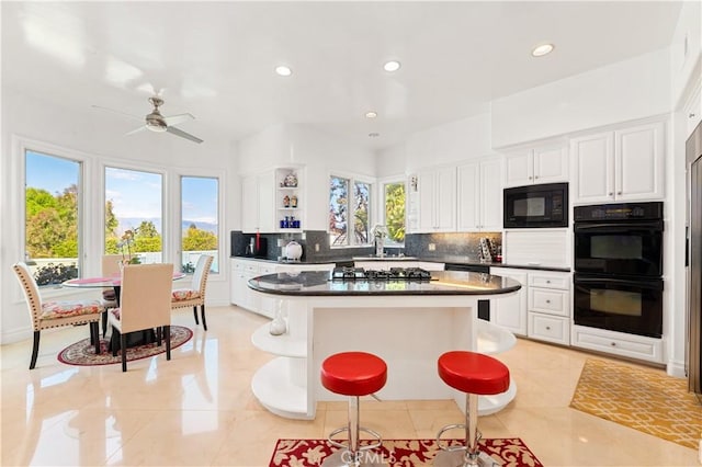 kitchen featuring white cabinets, black appliances, tasteful backsplash, ceiling fan, and a breakfast bar area