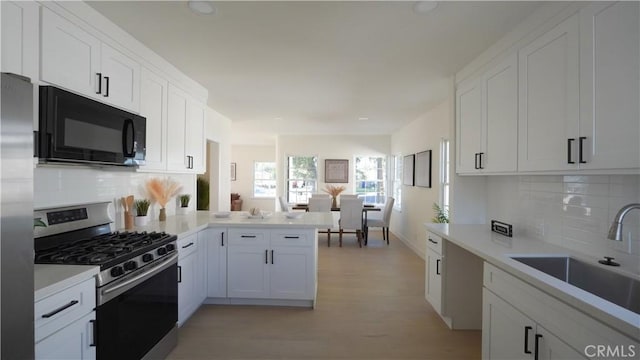 kitchen featuring kitchen peninsula, stainless steel appliances, tasteful backsplash, white cabinets, and sink