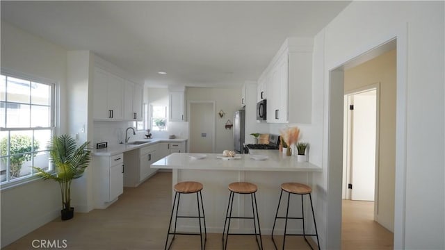 kitchen with kitchen peninsula, a breakfast bar area, appliances with stainless steel finishes, white cabinets, and sink