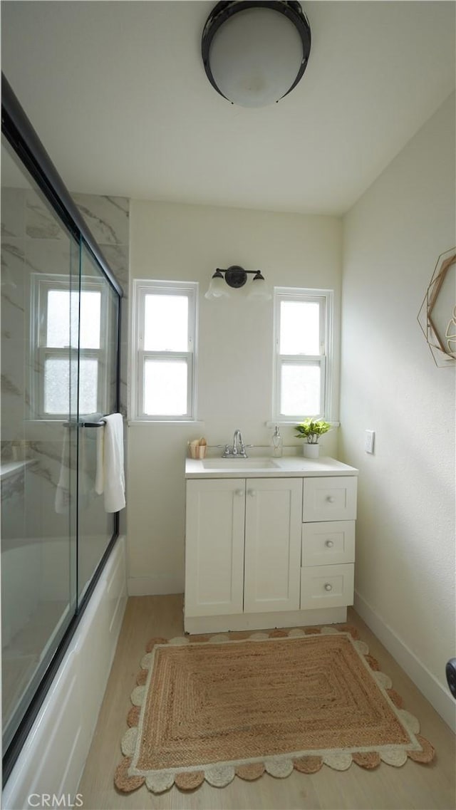 bathroom featuring a healthy amount of sunlight, wood-type flooring, vanity, and shower / bath combination with glass door