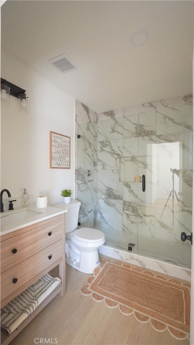 bathroom featuring hardwood / wood-style flooring, toilet, vanity, and a shower with shower door