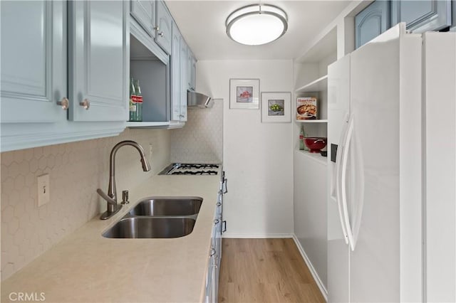 kitchen featuring sink, blue cabinetry, backsplash, light hardwood / wood-style floors, and white fridge with ice dispenser