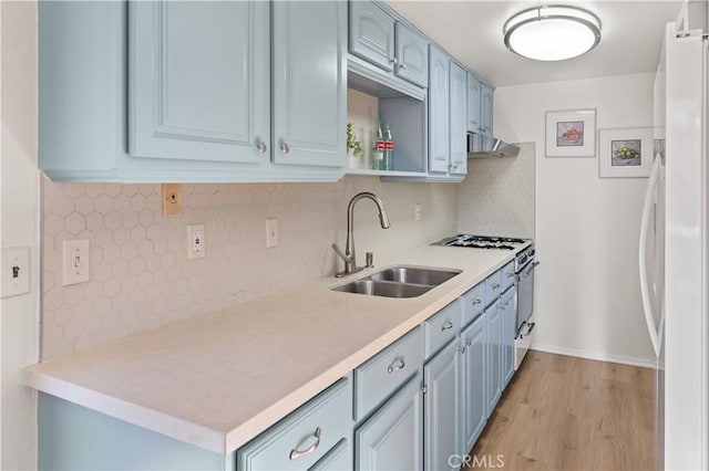 kitchen featuring stainless steel stove, sink, decorative backsplash, white fridge, and light wood-type flooring