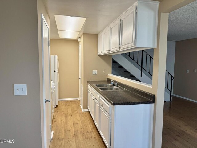 kitchen with white cabinetry, sink, white fridge, and light hardwood / wood-style flooring