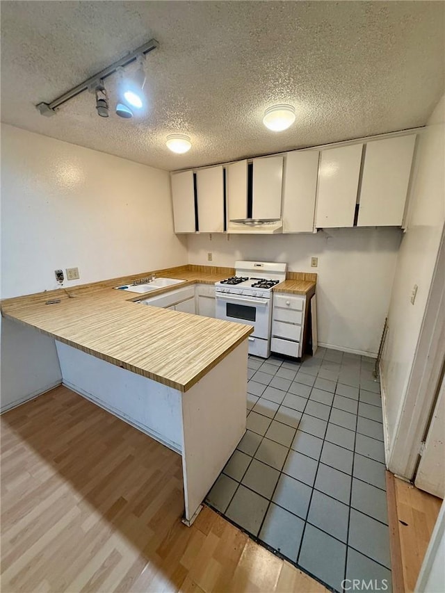 kitchen featuring a textured ceiling, white cabinetry, rail lighting, kitchen peninsula, and white gas range oven