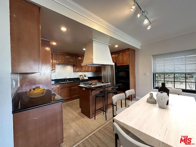 kitchen with premium range hood, black double oven, ornamental molding, a kitchen island, and sink