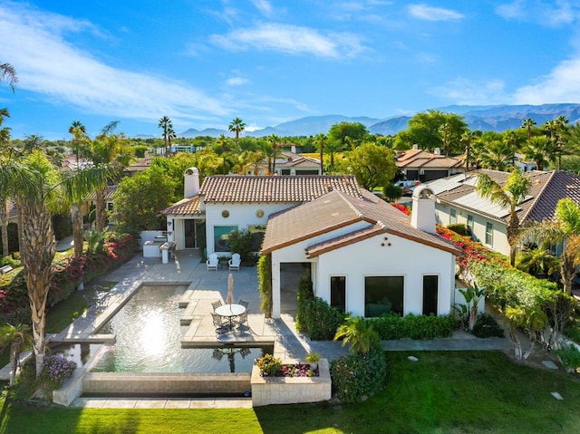 rear view of property with a patio, a mountain view, a yard, and an outdoor kitchen