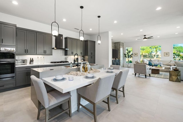 kitchen with wall chimney range hood, sink, a breakfast bar area, a spacious island, and decorative light fixtures