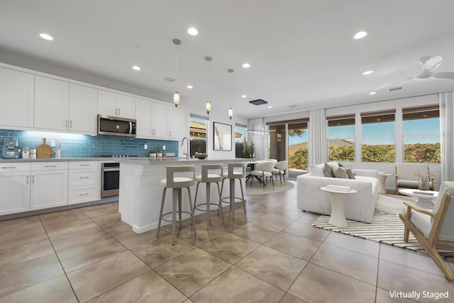 kitchen featuring white cabinetry, stainless steel appliances, backsplash, a kitchen island with sink, and pendant lighting